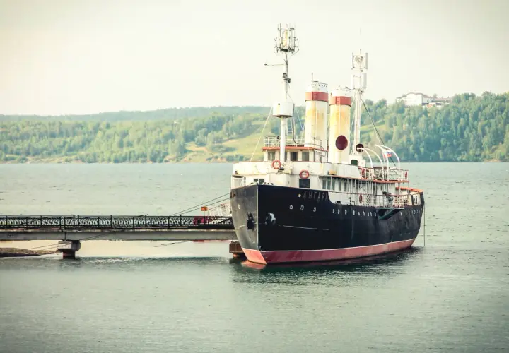 Stary statek "Angara" cumuje przy nabrzeżu. W tle zielone wzgórza i spokojna woda. Port nad Angarą.