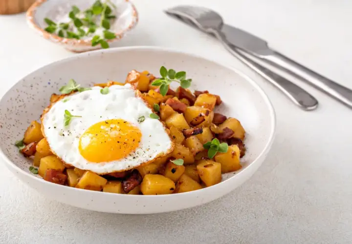 Un œuf au plat sur des pommes de terre sautées avec des lardons, une idée parfaite avec quoi accompagner des œufs pour un repas savoureux.