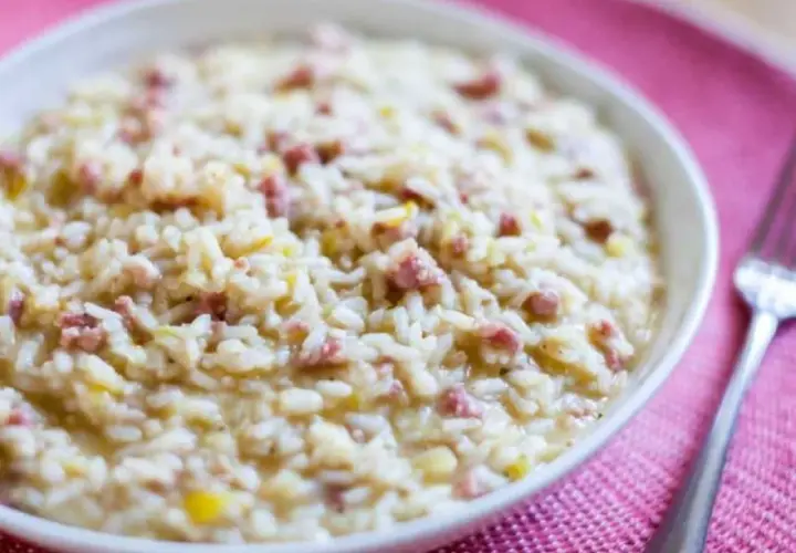 Un cremoso risotto salsiccia, con trocitos de salchicha italiana, servido en un cuenco blanco sobre un mantel rosa.