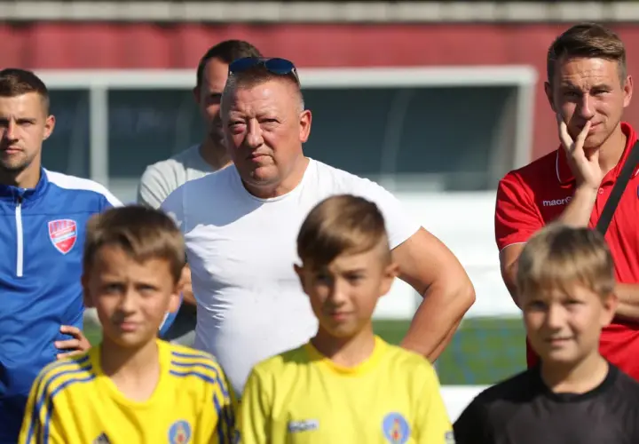 Marek Śledź, trener, w białej koszulce, stoi wśród młodych piłkarzy na boisku.