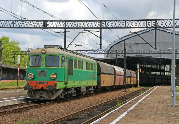 Zielona lokomotywa ST43-238 z wagonami towarowymi na torach kolejowych, pod zadaszeniem dworca.