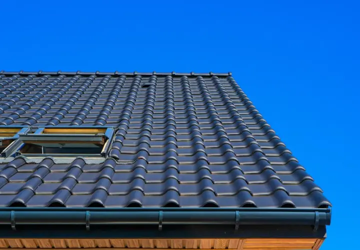 Toit en tuiles sombres, avec deux fenêtres de toit ouvertes, sous un ciel bleu vif. Ces matériaux de couverture sont bien posés.