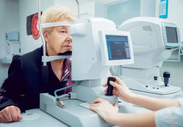 Starsza pani przechodzi badanie pola widzenia u okulisty. Aparatura diagnostyczna jest nowoczesna.