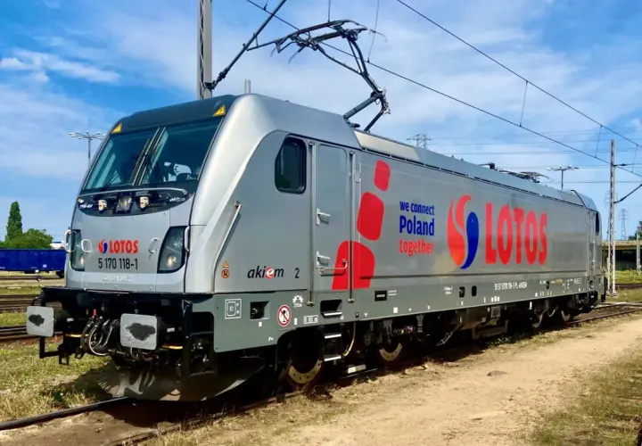 Srebrna lokomotywa Traxx z napisem LOTOS i hasłem "we connect Poland together" stoi na torach.