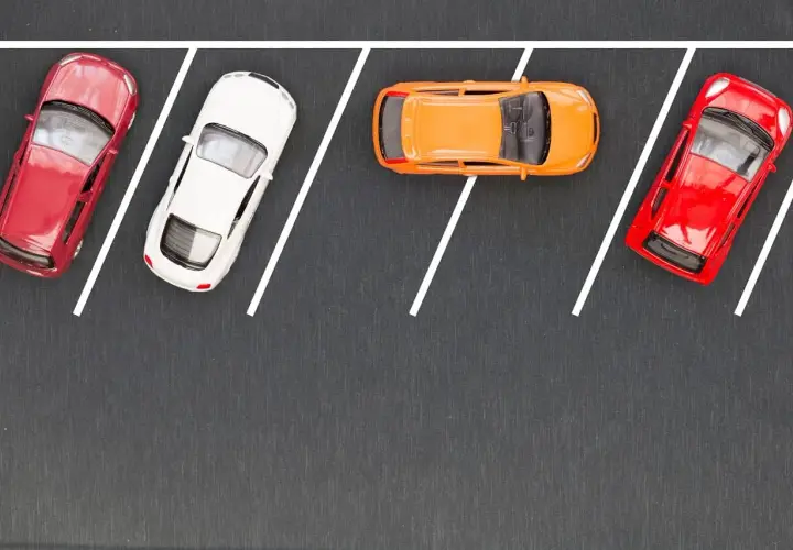 Cztery samochodziki: czerwony, biały, pomarańczowy i ponownie czerwony, zaparkowane na szarym tle z białymi liniami wyznaczającymi miejsca parkingowe.