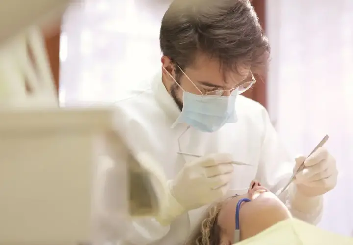 Dentysta w masce i rękawiczkach wykonuje zabieg. Pacjentka leży na fotelu. Pytanie o ile l4 po wyrwaniu ósemki.