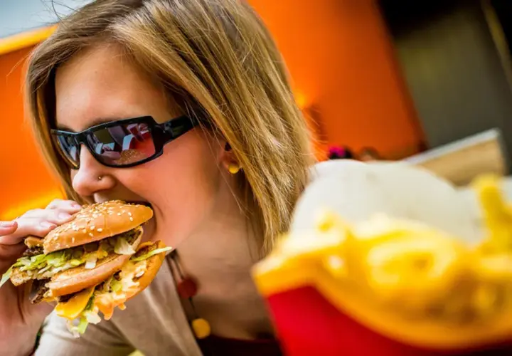 Dziewczyna w okularach je pysznego mcmuffin wieprzowy z jajkiem. Obok frytki.