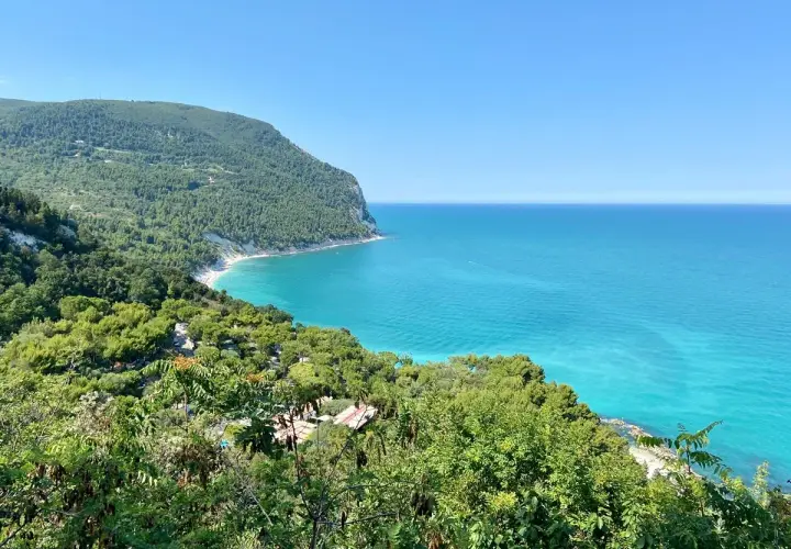 Vista mozzafiato sulla costa marchigiana, un gioiello tra le 10 cose da vedere nelle Marche. Mare turchese e verde lussureggiante.