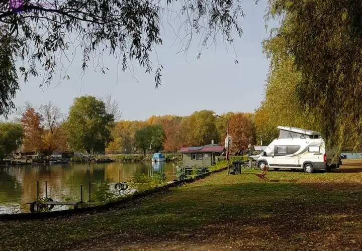 Jesień na Węgrzech. Kamper zaparkowany nad jeziorem, w tle kolorowe drzewa i mała chatka.