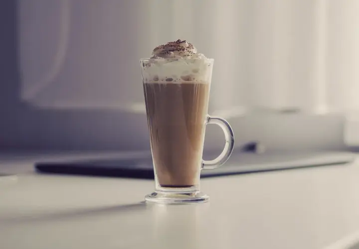 Jak zrobić latte macchiato? Wysoka szklanka z kawą, mlekiem i bitą śmietaną, posypana kakao. Idealny napój na chłodne dni.