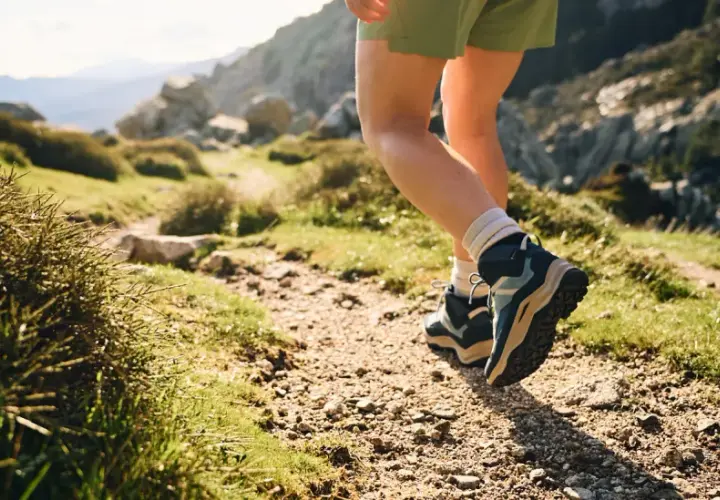 Hiking boots, one leather, one synthetic, tread a rocky path through a sun-drenched mountain landscape.