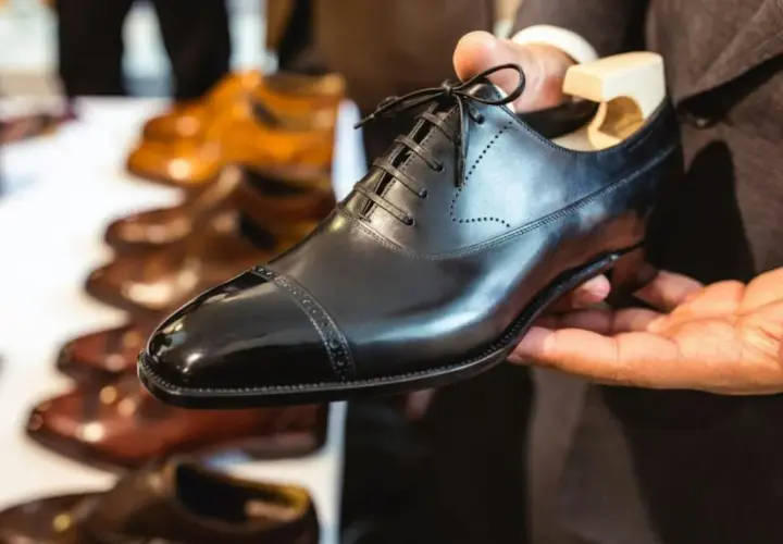 Main d'un homme tenant une chaussure noire brillante, prête à nourrir le cuir. D'autres chaussures en cuir sont alignées en arrière-plan.
