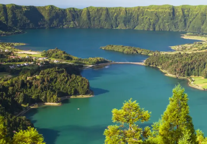 Malowniczy krajobraz portugalskiego archipelagu na Atlantyku: jezioro w kraterze wulkanicznym, otoczone zielonymi wzgórzami i niewielką wioską.