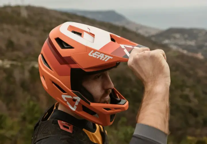 Uomo con casco integrale Leatt arancione, pronto per downhill. Il casco integrale significato è protezione totale.