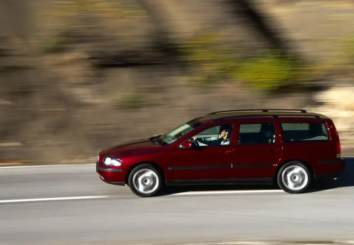 Czerwone volvo v70 ii jedzie po drodze, za kierownicą siedzi kobieta. Rozmyte tło sugeruje ruch.