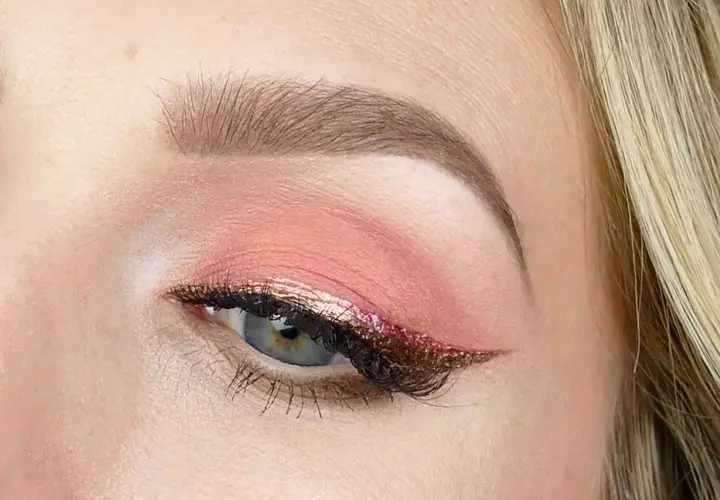 En närbild på ett öga med en vacker rosa sminkning. Ögonlocket har en mjuk rosa skugga och en glittrig eyeliner i guld och rosa.