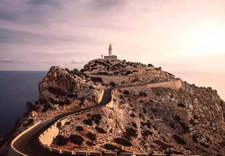 Faro en la cima de un acantilado rocoso, con una carretera serpenteante que asciende. Un paisaje de monumentos naturales impresionantes.