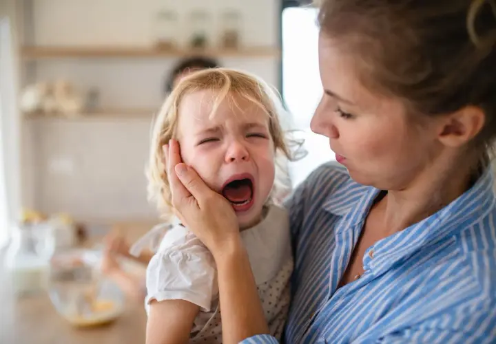 Madre consuela a su hija de 3 años en medio de berrinches. La niña llora desconsoladamente mientras su madre la abraza con ternura.