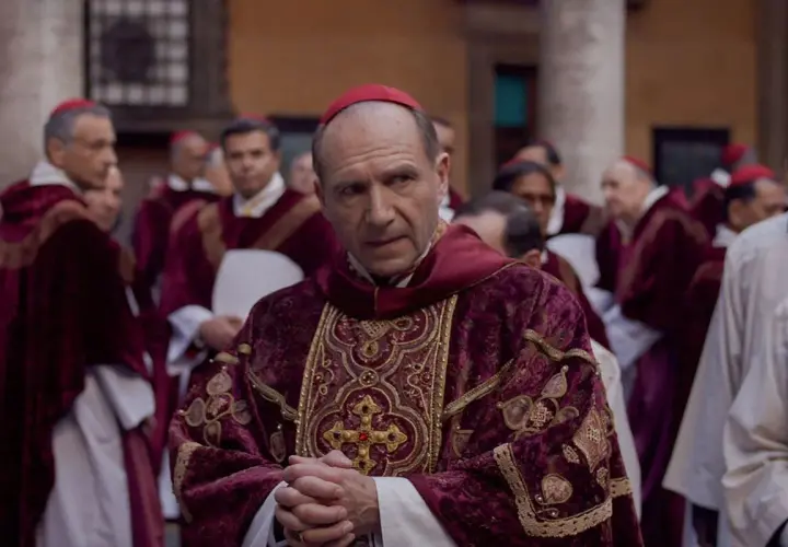 Scena z filmu o papieżu. Kardynał w bogato zdobionej szacie z czerwonym piuską. W tle inni duchowni.