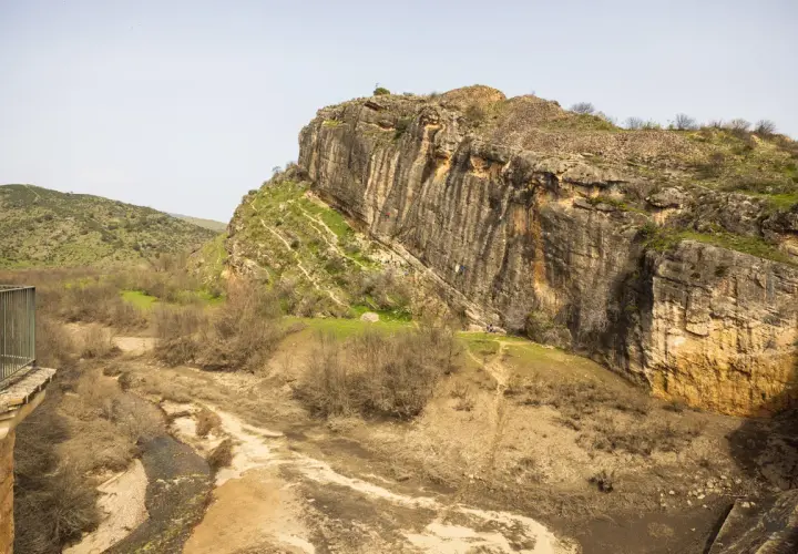 Escalada en la **ruta cañones del rio lozoya**. Un paisaje rocoso con un río seco y vegetación escasa.