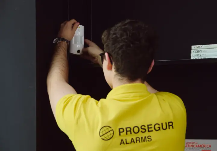 Técnico instala un sensor PIR blanco en una estantería, asegurando la protección del hogar.