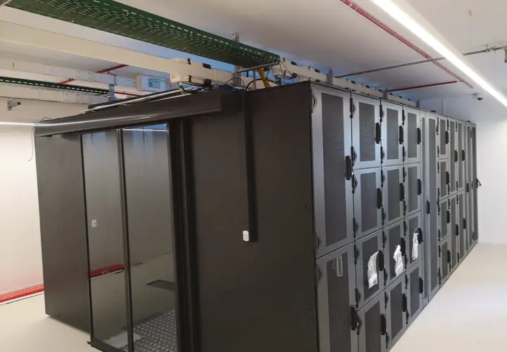 Un micro data center avec des baies de serveurs noires et une porte vitrée. Des câbles et des conduits sont visibles au plafond.