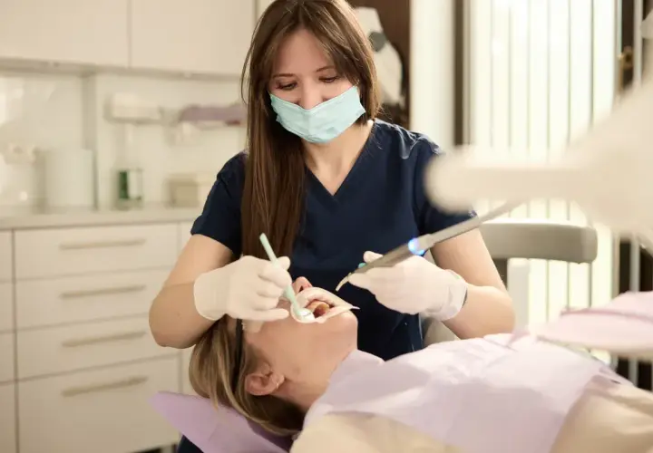 Dentystka w masce i rękawiczkach wykonuje zabieg. Szukasz najlepszych klinik stomatologicznych w Warszawie?