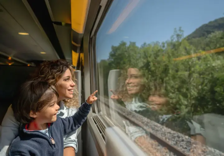 Bambino e madre guardano fuori dal finestrino del treno, indicando qualcosa. Un'ottima idea per i giochi da fare in treno, osservando il paesaggio che scorre.