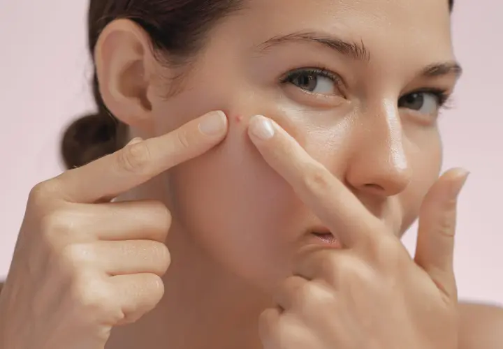 Une jeune femme examine un bouton sur sa joue, un signe possible pour savoir si on a une peau grasse.