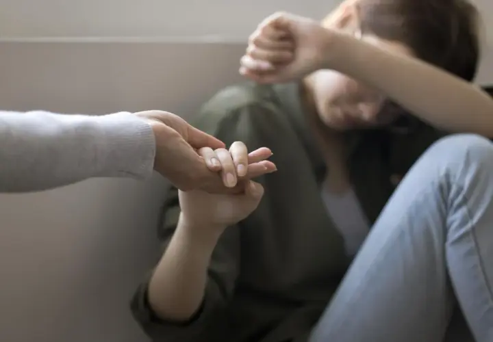 Dłoń wyciągnięta do osoby skulonej, zakrywającej twarz.