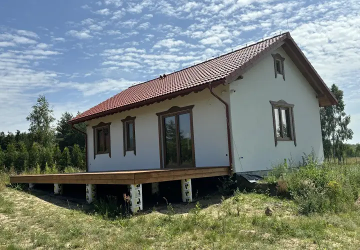 Nowy projekt domu drewnianego z tarasem, w otoczeniu zieleni.