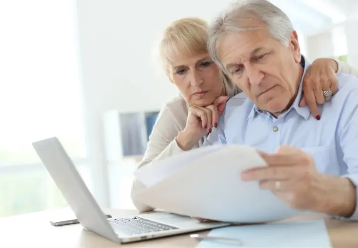 Zmartwieni seniorzy analizują dokumenty dotyczące emerytury pomostowej przy laptopie.