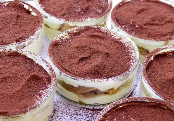 Varios vasitos de tiramisú, con capas de crema y bizcocho, espolvoreados con cacao. Los tiramisú ingredientes se ven deliciosos.