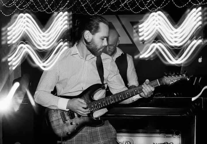 Muzyk gra na gitarze elektrycznej. Efekt świetlny na zdjęciu to długie naświetlanie, które pokazuje ruch świateł. Ekspozycja co to? To czas, przez który matryca aparatu jest naświetlana.