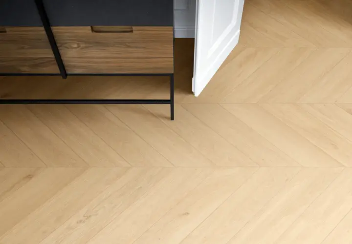 Posa di un elegante parquet in gres porcellanato effetto legno, con un motivo a spina di pesce che si estende verso una porta bianca aperta.