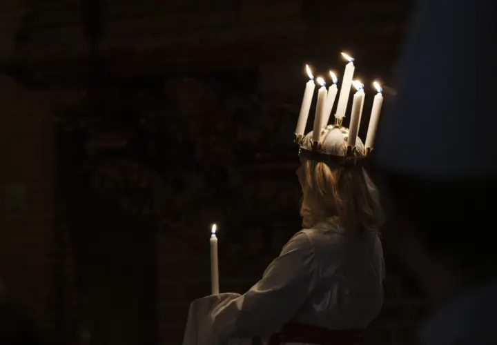 En flicka med ljus i håret, en traditionell Storkyrkan Lucia, håller ett ljus i mörkret.