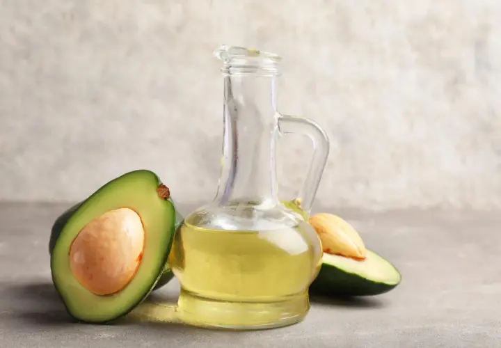 Bouteille en verre remplie d'huile avocat dorée, avec des moitiés d'avocat frais autour.