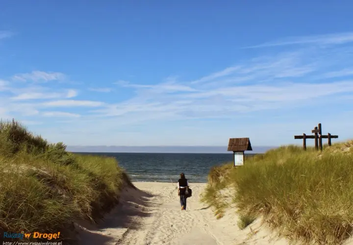 Kobieta idzie piaszczystą ścieżką na plażę. To idealne miejsce na chwilę wytchnienia podczas podróży samochodem.