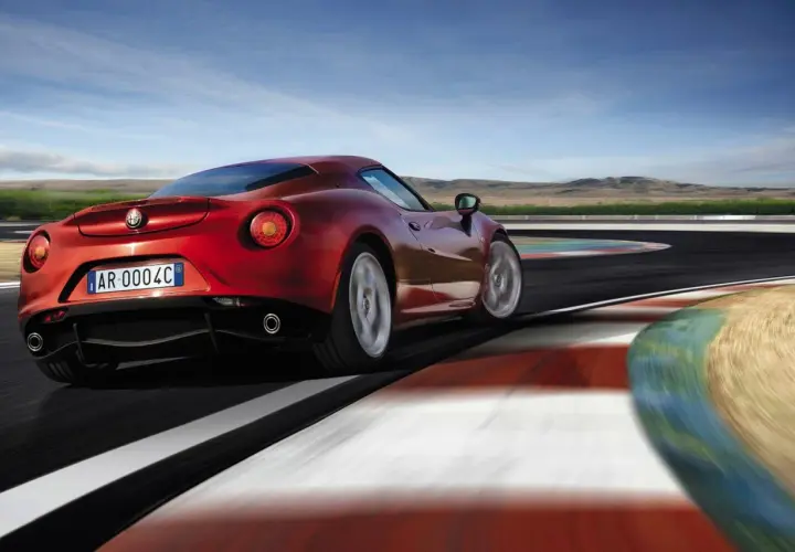 Czerwone Alfa Romeo 4C na torze wyścigowym, z rozmytymi kołami i kolorowymi bandami.
