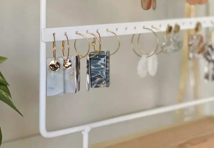 Un porta pendientes blanco exhibe varios pares de aretes colgantes, algunos con detalles dorados y otros con diseños marmoleados.