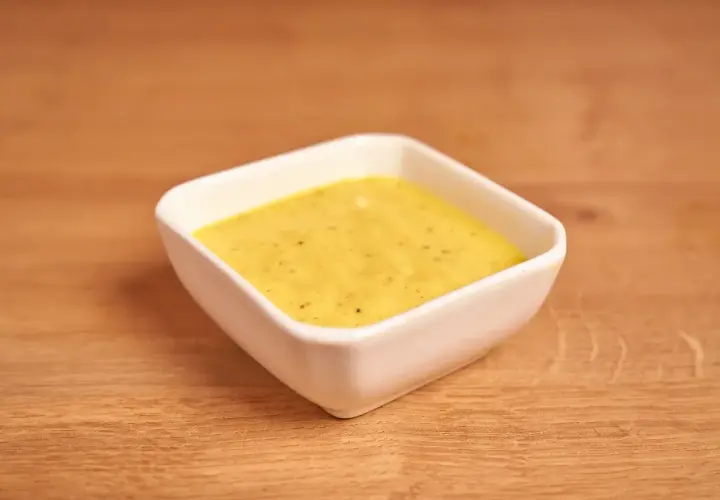 Un cuenco blanco contiene una cremosa salsa miel y mostaza, lista para acompañar tus platos.