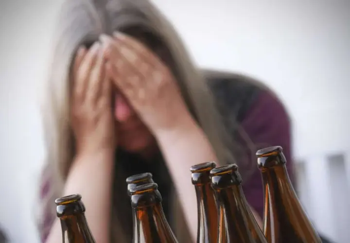 Verzweifelte Frau mit Händen vor dem Gesicht, umgeben von Bierflaschen. Ein Symbol für die Gefahren von Alkohol und die mögliche Entwicklung von Alkohol-Demenz.