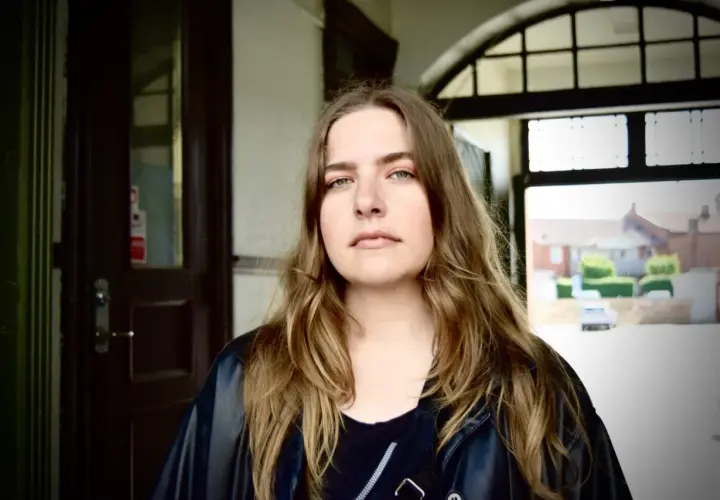 Miriam Ingrid, med sitt långa, vågiga hår och gröna ögon, blickar ut från en mörk port.