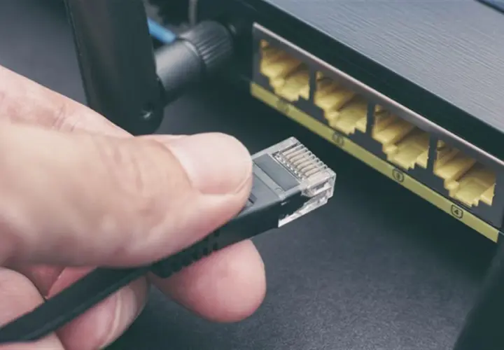 Main d'une personne tenant un câble rj45, prêt à le brancher dans un routeur. Connexion réseau.