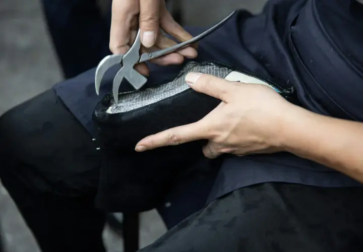 Mains expertes utilisant un outil pour réparer le simili cuir qui s'effrite sur un objet noir.