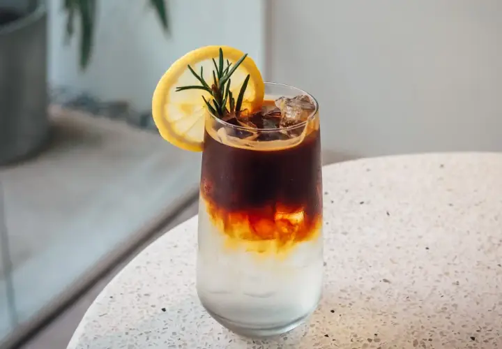 Orzeźwiający tonic espresso z plasterkiem cytryny i rozmarynem, idealny na upalny dzień.