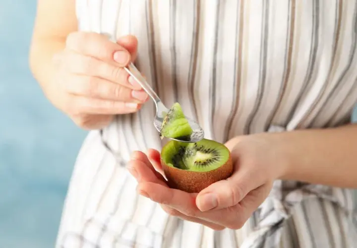 Kobieta trzyma w dłoniach połówkę kiwi i łyżeczkę z kawałkiem owocu.