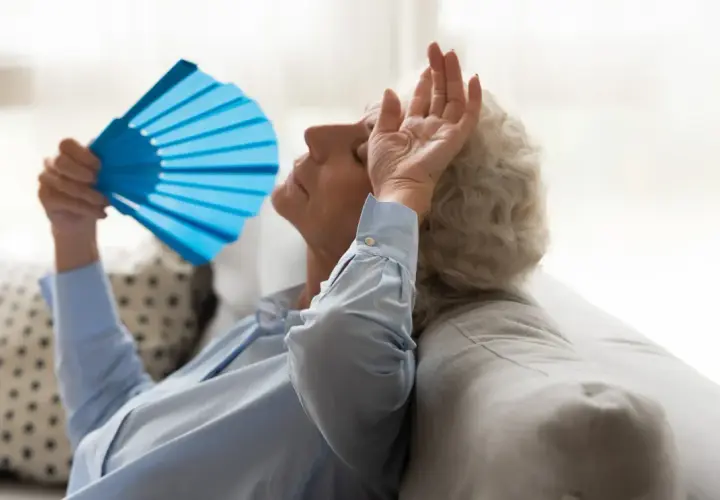 Une femme âgée s'évente avec un éventail bleu, montrant les effets de la chaleur sur les personnes âgées.