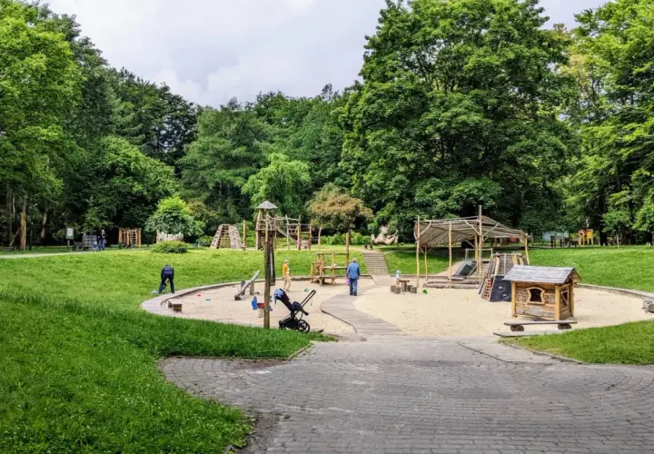 Plac zabaw w parku Kościuszki, otoczony zielenią, z piaskownicą, zjeżdżalniami i domkiem dla dzieci.