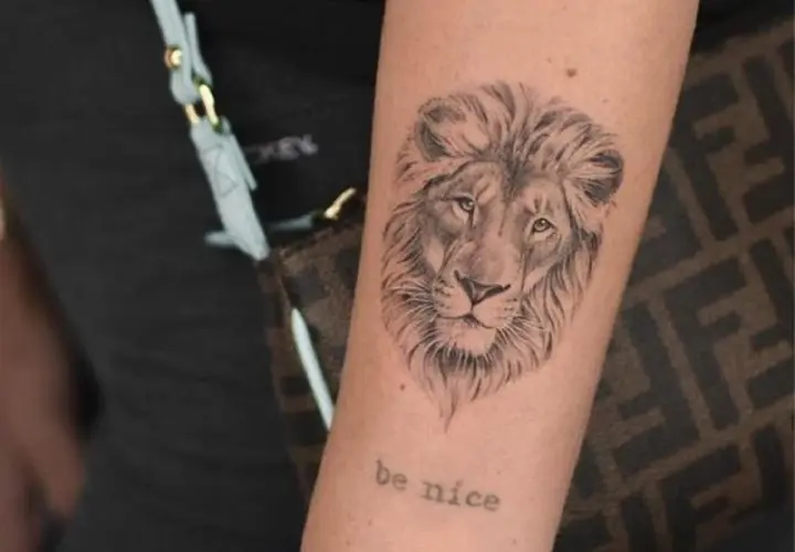 Tatuaż znak zodiaku lew na ramieniu, z napisem "be nice" poniżej.